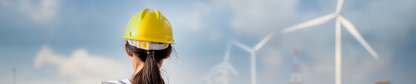 Woman engineer or architect with white safety hat and wind turbines on background