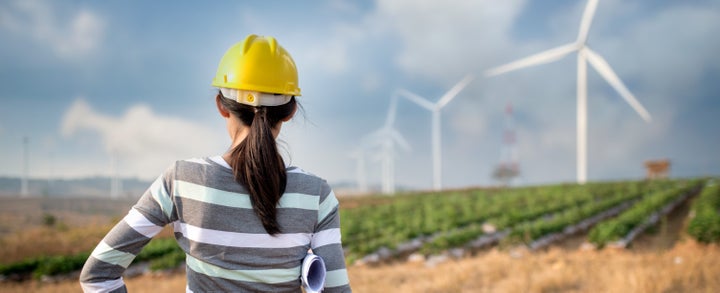 Woman engineer or architect with white safety hat and wind turbines on background